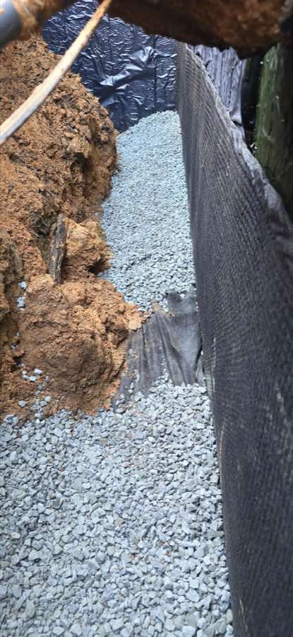 Clean drainage stone and separation fabric installed beside an exterior foundation membrane