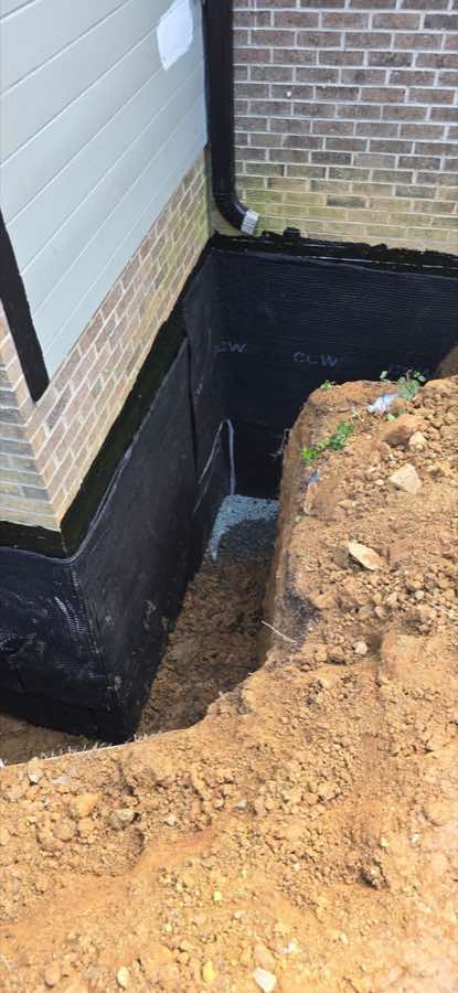 Authentic exterior foundation waterproofing process with excavation, wall coating, and protection membrane visible